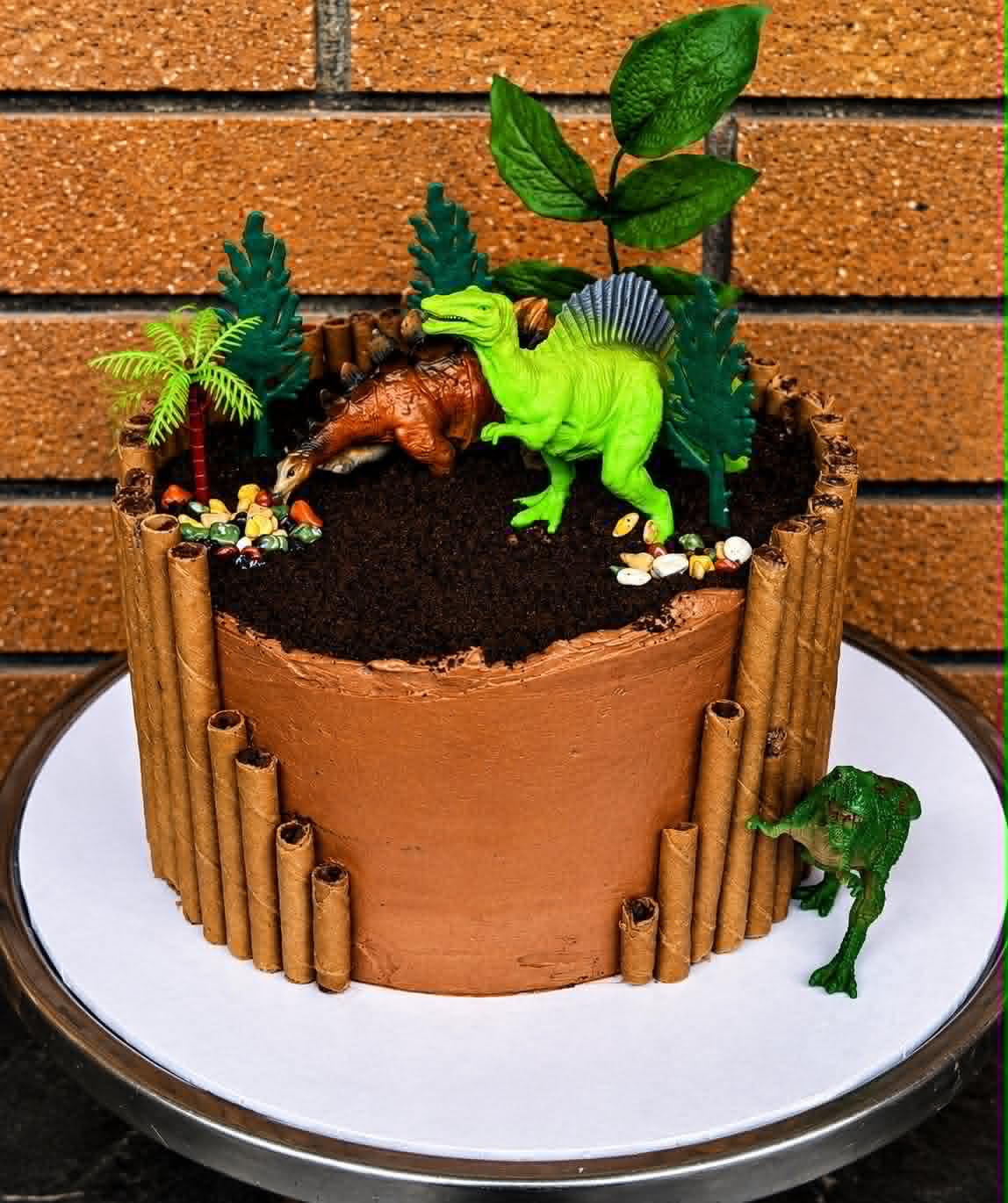 Chocolate dinosaur jungle cake with wafer roll border, dinosaur figurines and tropical foliage on top